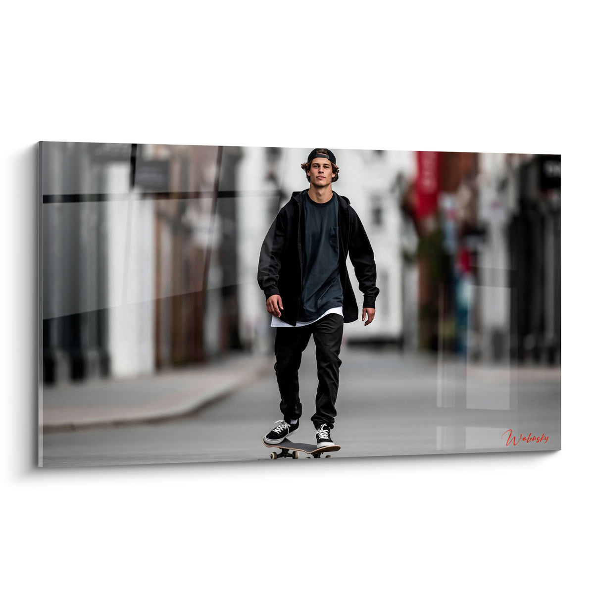 Skateur en tenue noire glisse sur une planche, rue grise et blanche floutée en arrière-plan