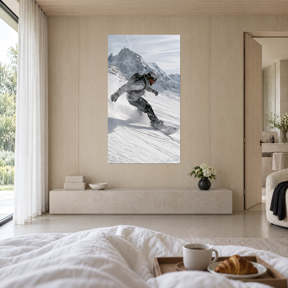 Wall art snowboarder carving down the slope, black gloves and tinted goggles, grey rocky ridge under blue sky, above a bed in a bright bedroom