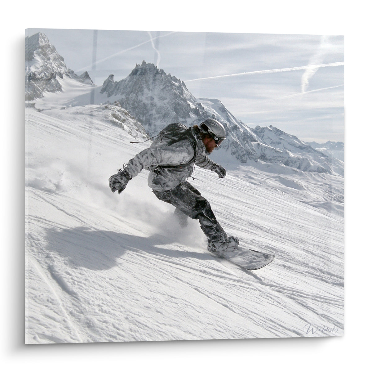 Snowboardeur en combinaison grise dévalant une pente blanche face aux sommets rocheux