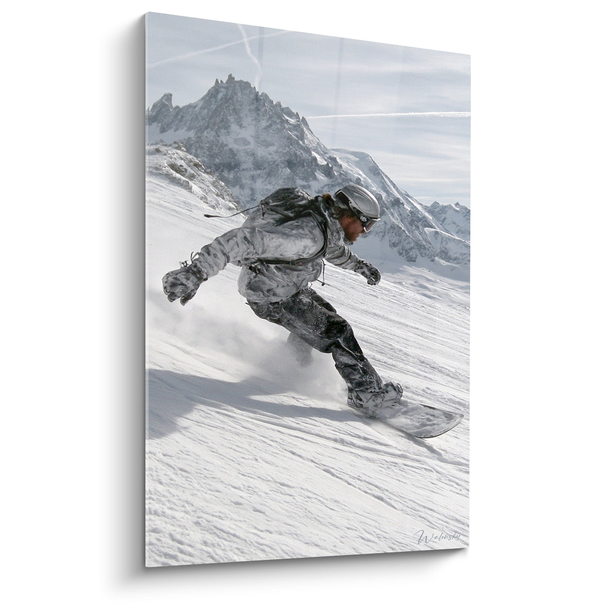 Snowboardeur en tenue grise dévalant une pente blanche face à des sommets anthracite