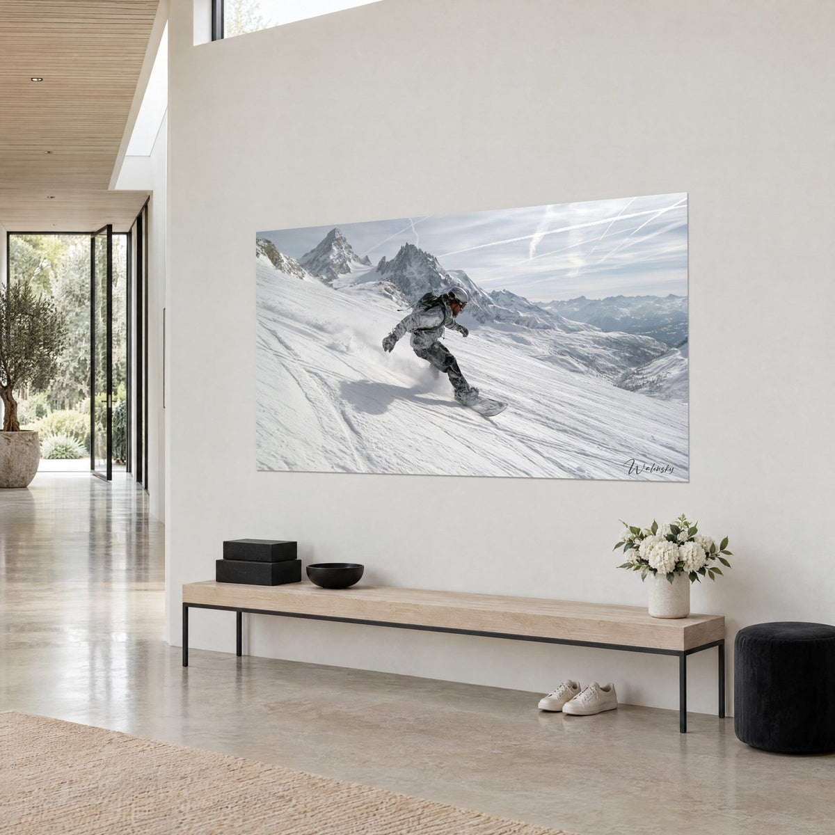Cuadro de un rider con casco trazando una curva en la nieve polvo blanca, agujas rocosas grises y cielo azul pálido, pared crema de una casa de arquitecto