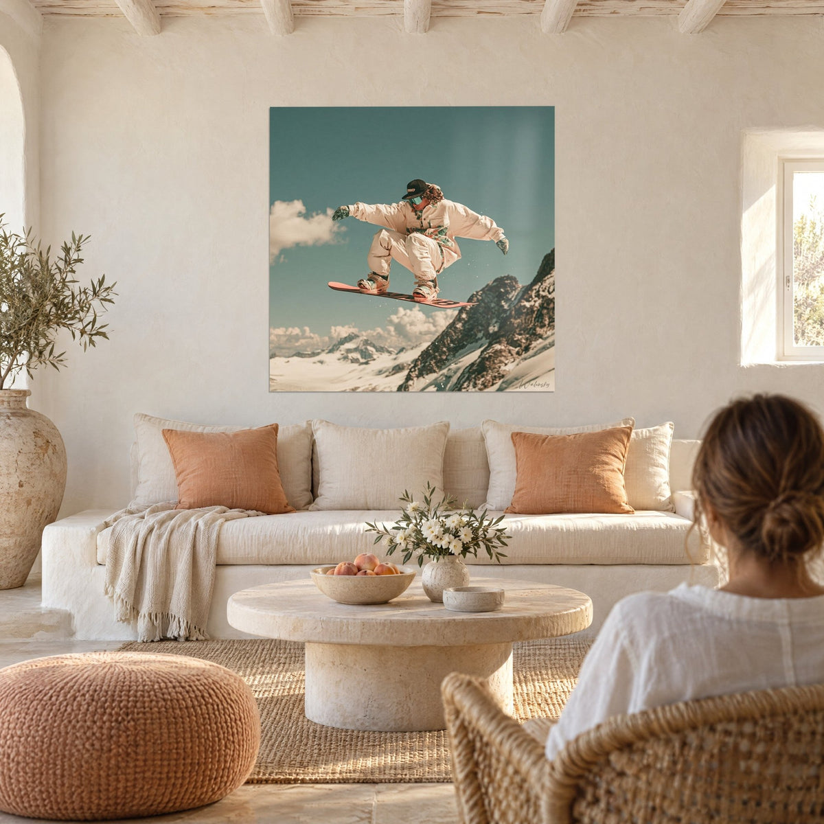 Quadro snowboarder beige in pieno salto, tavola corallo, cielo turchese, due persone di spalle sopra un divano in un soggiorno luminoso