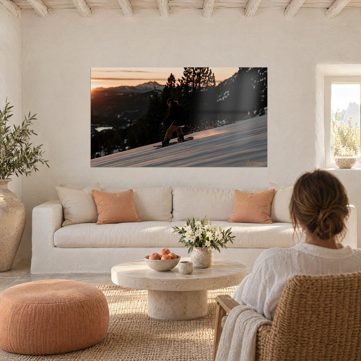 Wall art snowboarder in black beanie and orange pants gliding over pink snow at sunset, above a sofa in a bright living room