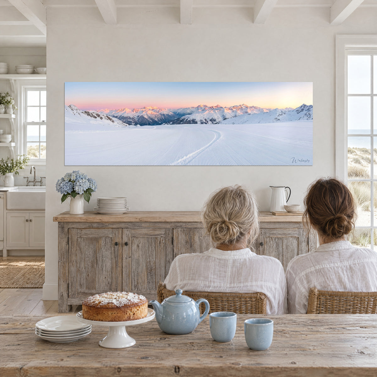 Wall art fresh snow tracks in the early morning, pink ridges and glacier blue, facing a whitewashed wooden table with a cake