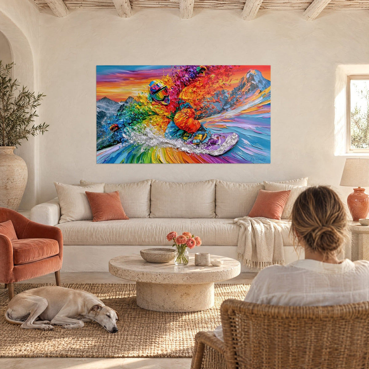 Wall art of an orange and purple snowboarder spraying snow, couple seen from behind and a greyhound, above a sofa in a bright living room