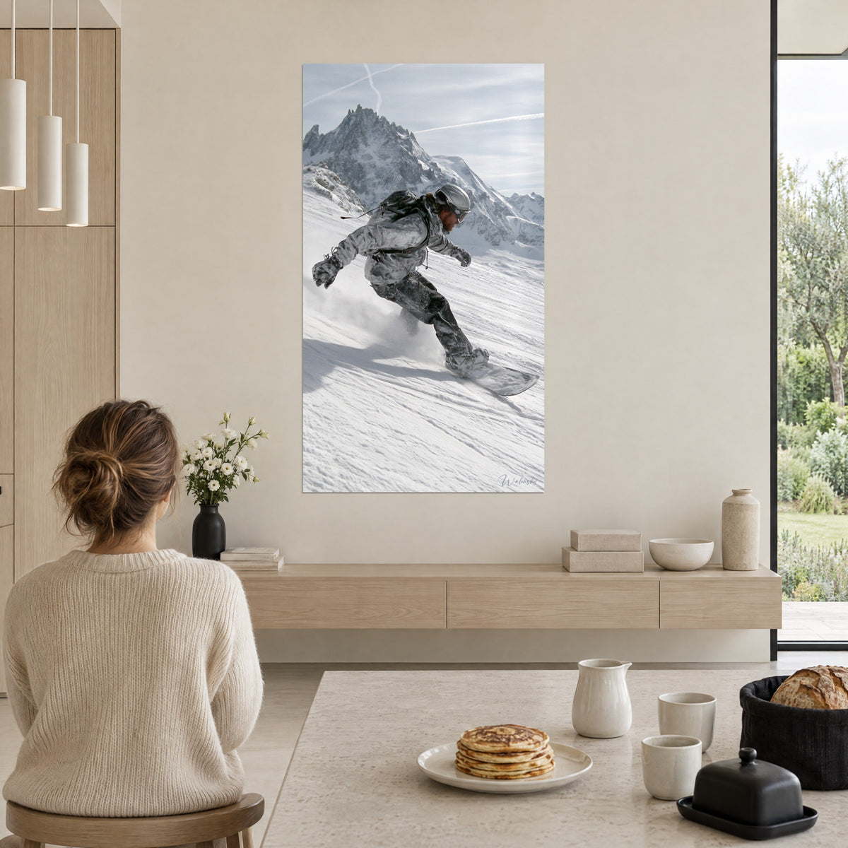 Wall art snowboard turn kicking up a cloud of white snow, grey silhouette facing bluish mountains, beige wall beside a breakfast table