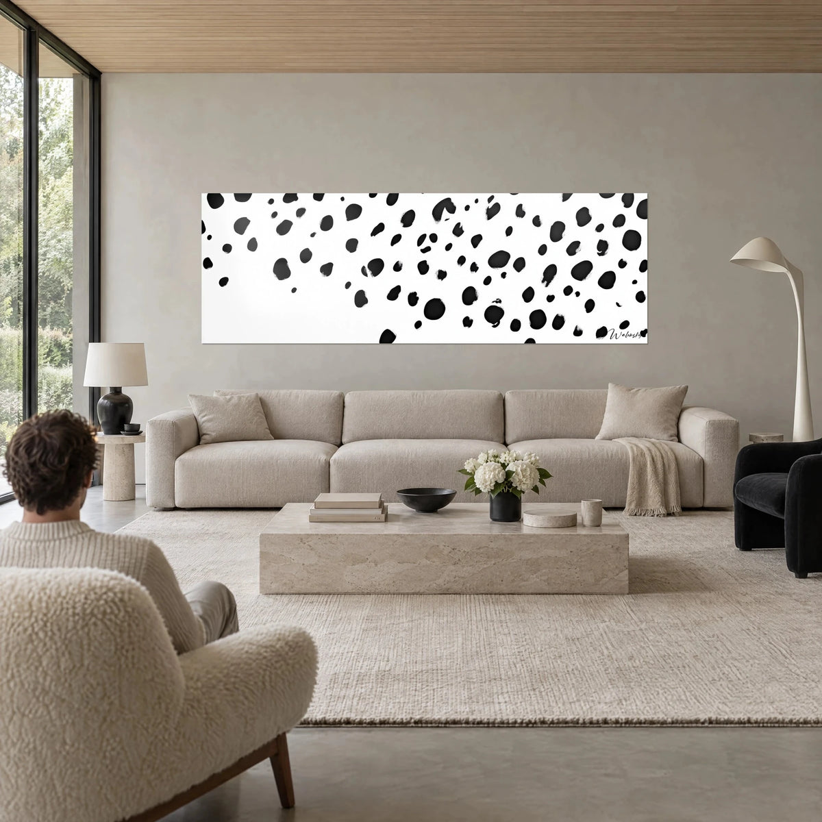 Wall art with scattered black spots on white background, panoramic format, hung on grey wall above a sofa in a bright living room