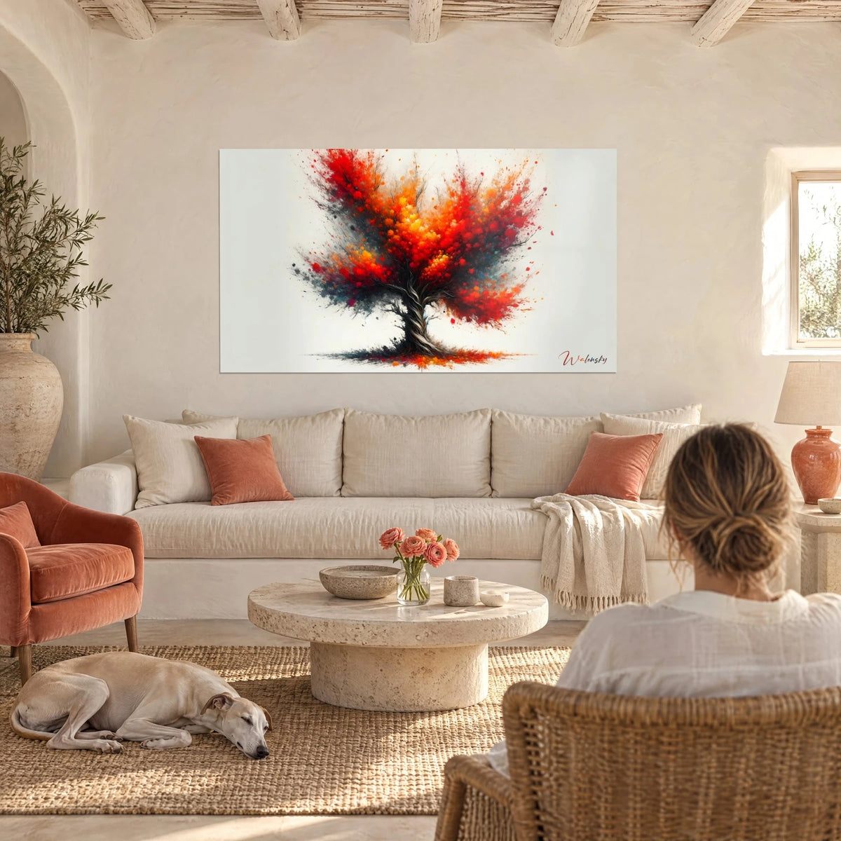 Wall art blazing tree with vermilion red and orange foliage, twisted black trunk, a woman seen from behind and a greyhound above a sofa in a bright living room