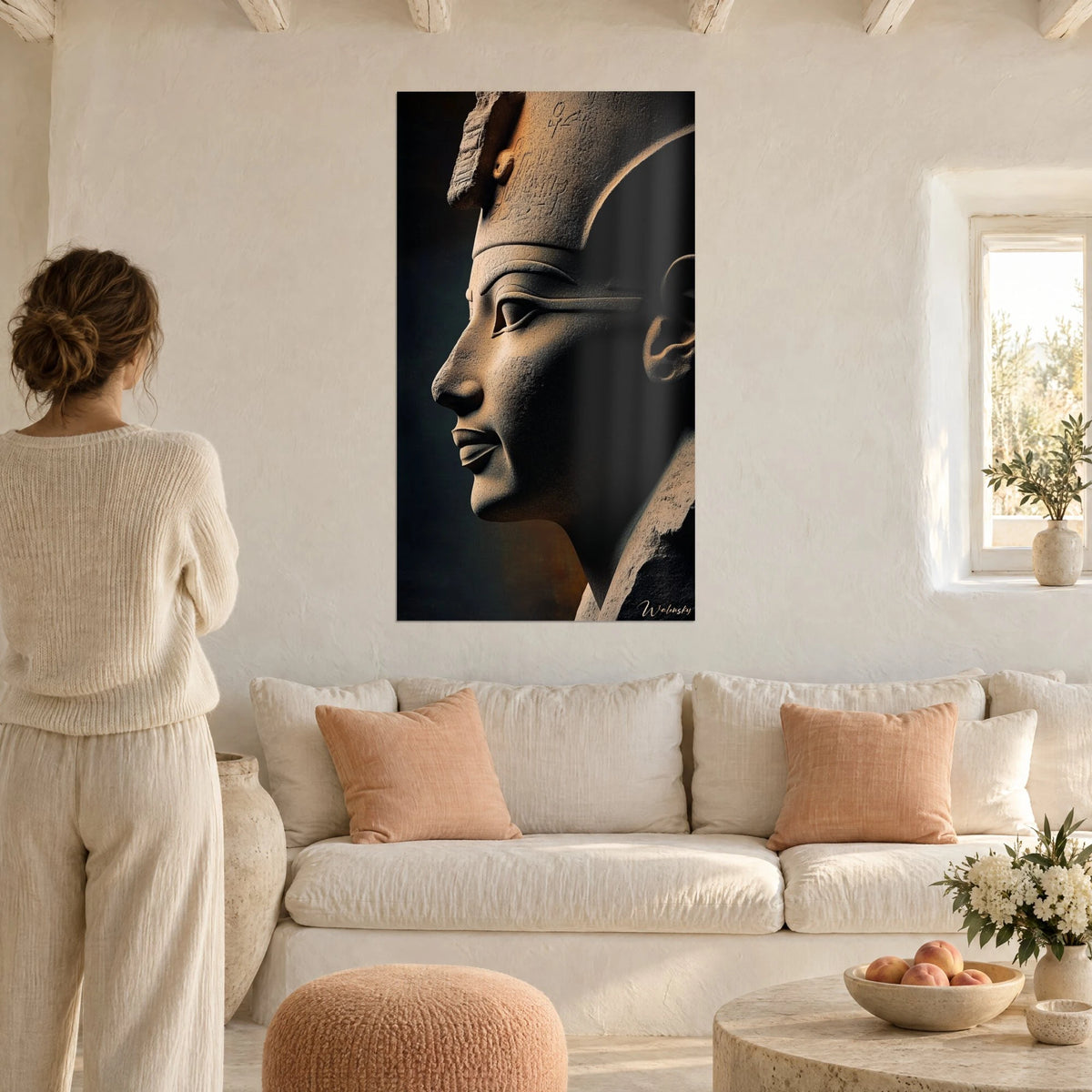 Gemälde mit grauem Steinprofil einer Sphinx, bronzene Schatten und nachtblauer Hintergrund, Frau von hinten, über einem Sofa in einem hellen Wohnzimmer