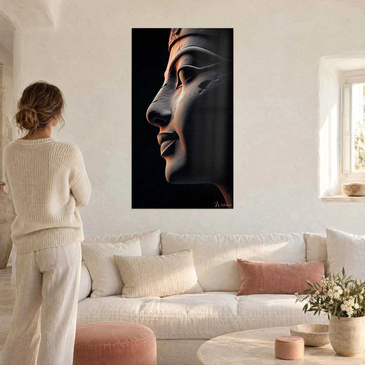 Quadro profilo scolpito di faraone, pietra grigia con riflessi arancio su fondo nero, donna di spalle sopra un divano in un soggiorno luminoso