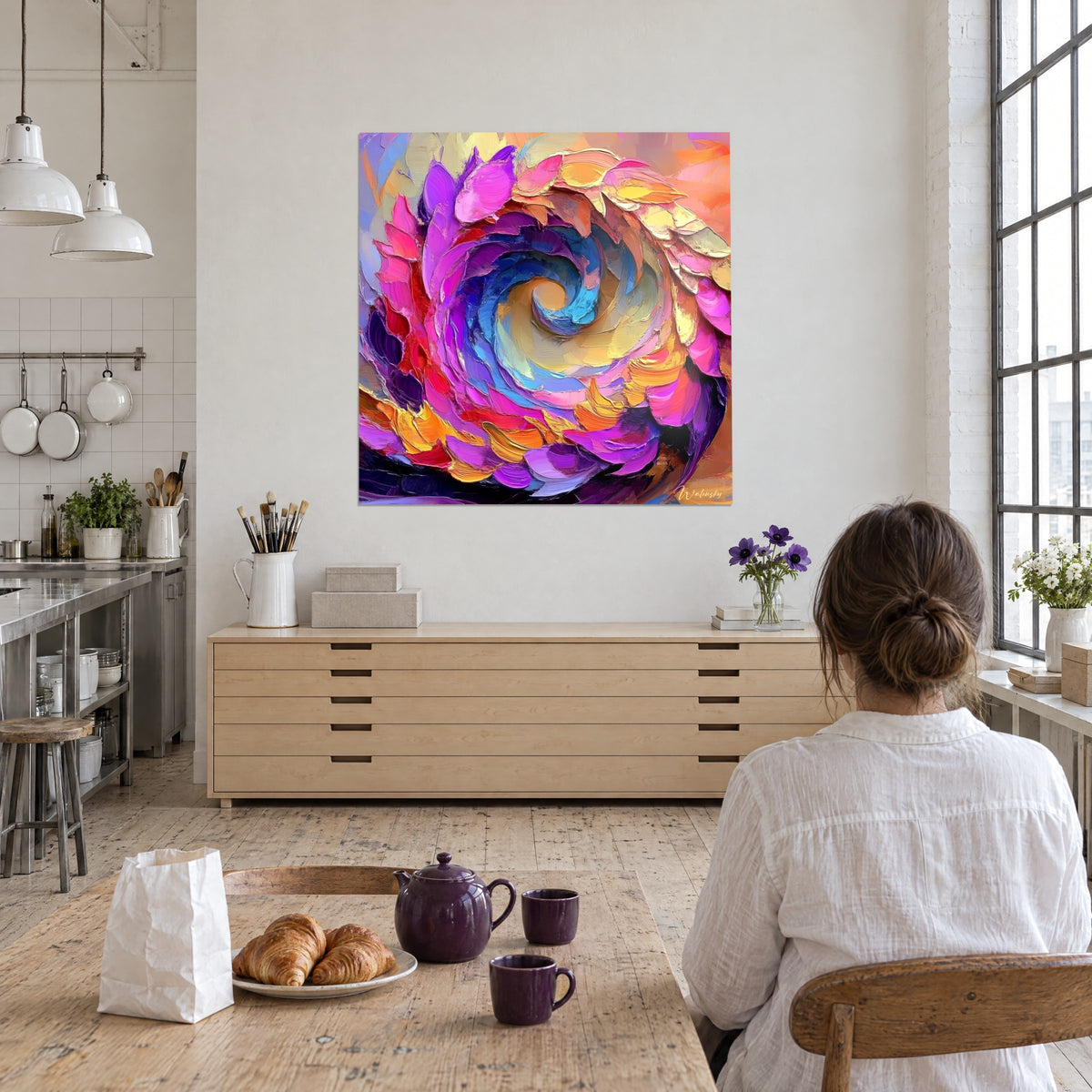 Gemälde mit spiralförmiger Blüte in Orange, Violett und Gelb, gegenüber einer am Tisch sitzenden Frau von hinten in einem Backsteinloft