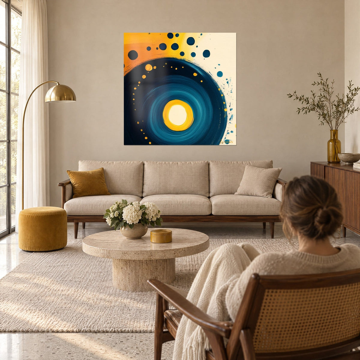 Wall art midnight blue spiral outlined with mustard yellow dots, cream center, woman seen from behind, above a sofa in a bright living room