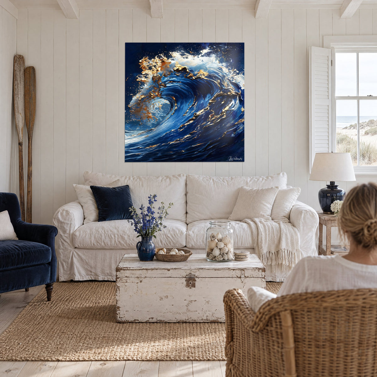 Tableau vague bleu nuit ourlée d'écume dorée, deux personnes de dos au-dessus d'un canapé dans un salon lumineux