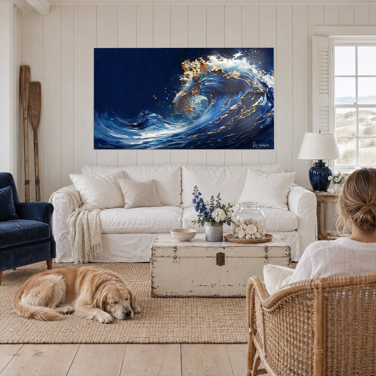 Tableau déferlante bleu marine ourlée d'or et d'écume blanche, deux personnes de dos, au-dessus d'un canapé dans un salon lumineux