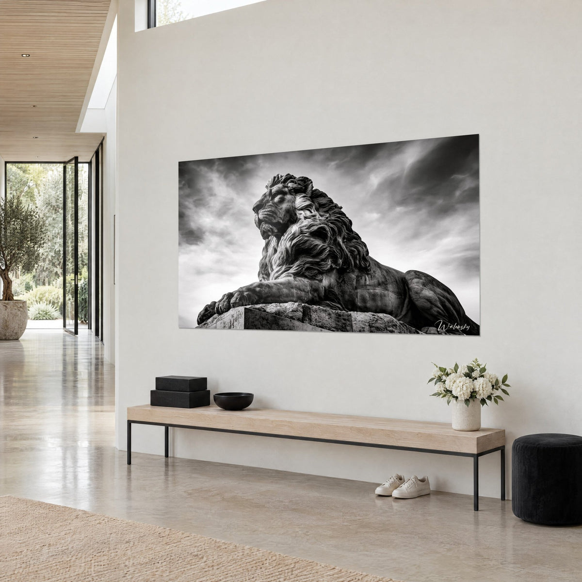 Quadro felino disteso sul suo piedistallo di pietra, cielo nuvoloso grigio e bianco, zampa in avanti, visto di tre quarti su parete beige