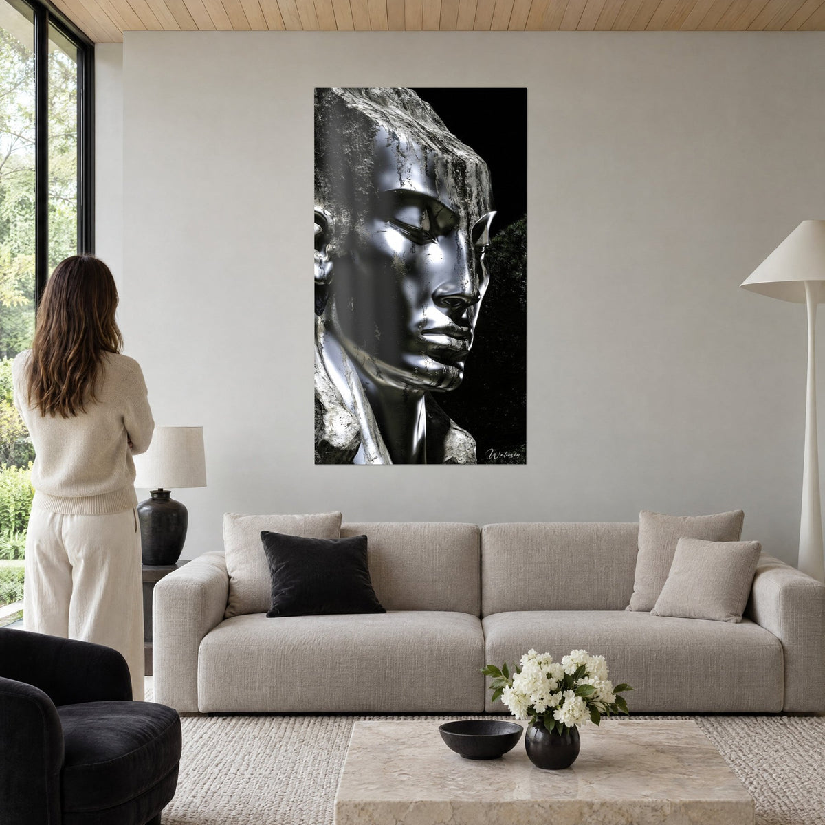 Wall art silver-faced statue, closed eyes, raw grey face on black background, woman seen from behind, above a sofa in a bright living room