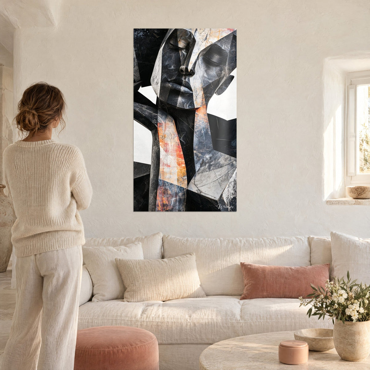 Cuadro rostro escultural de planos angulosos en gris antracita y ocre naranja, mujer de espaldas, sobre un sofá en un salón luminoso