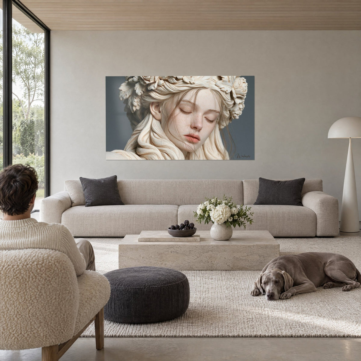 Tableau visage de marbre ivoire aux paupières closes, mèches dorées et couronne de feuilles, fond gris-bleu, au-dessus d'un canapé dans un salon lumineux