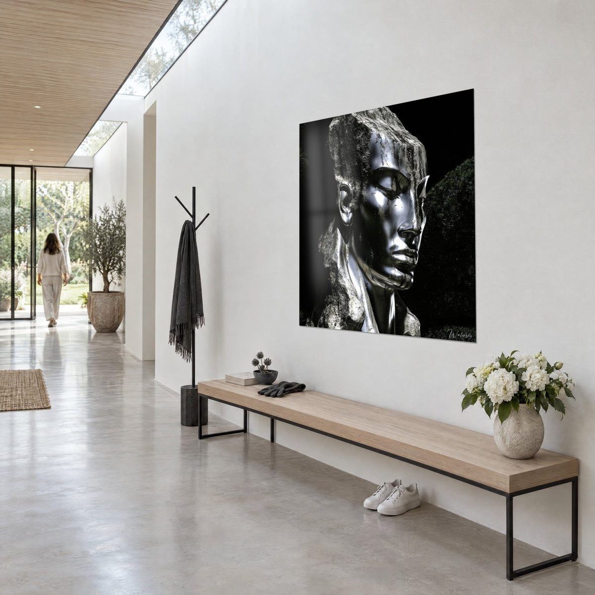 Quadro busto metallico argentato che emerge da un blocco di pietra grigia, sfondo nero profondo, su una parete bianca di un corridoio vetrato