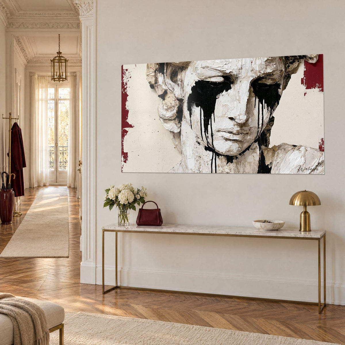 Tableau visage de statue en relief crème, coulures noires sous les yeux et pans bordeaux, au-dessus d'une console dorée