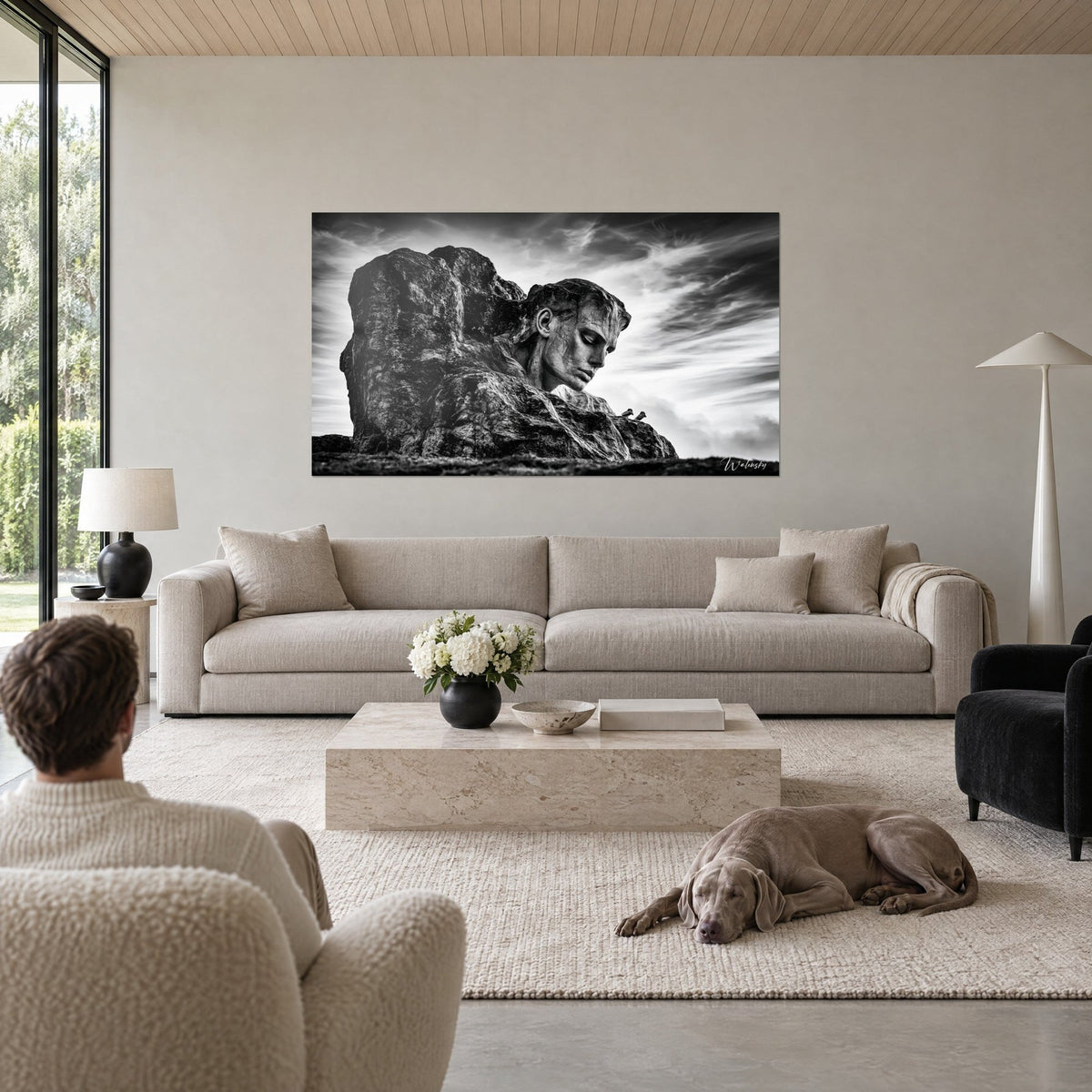 Tableau visage de pierre émergeant d'un rocher en noir et blanc, ciel strié de nuages, au-dessus d'un canapé dans un salon lumineux