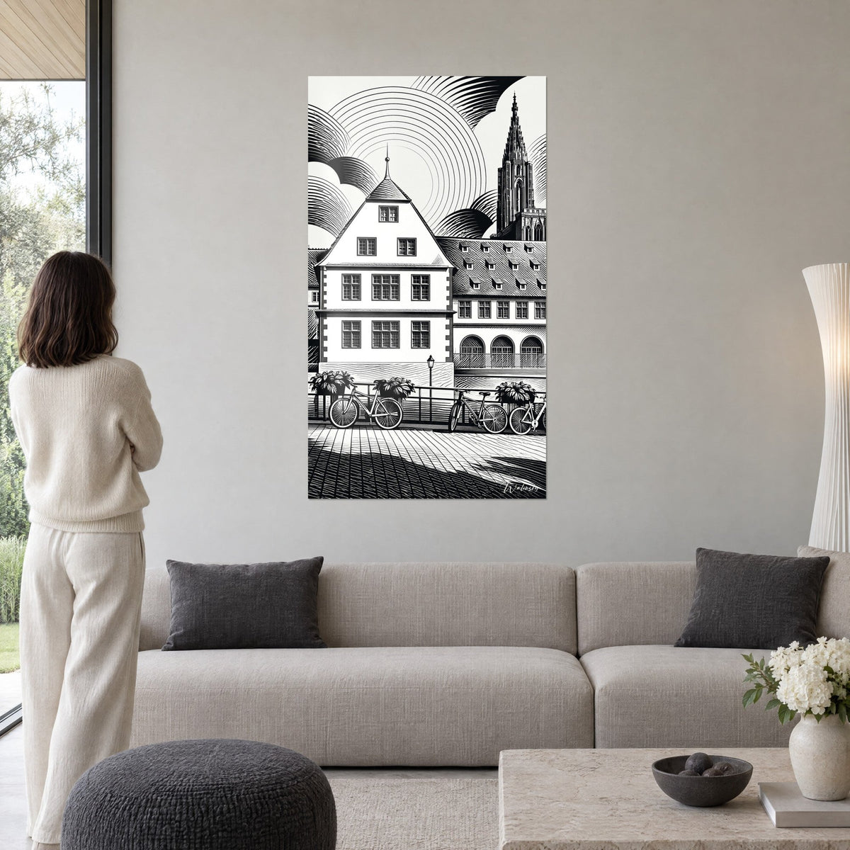 Schilderij witte Elzasser woning met puntgevel en kathedraal, zwart-witte gravure, vrouw van achteren, boven een bank in een lichte woonkamer