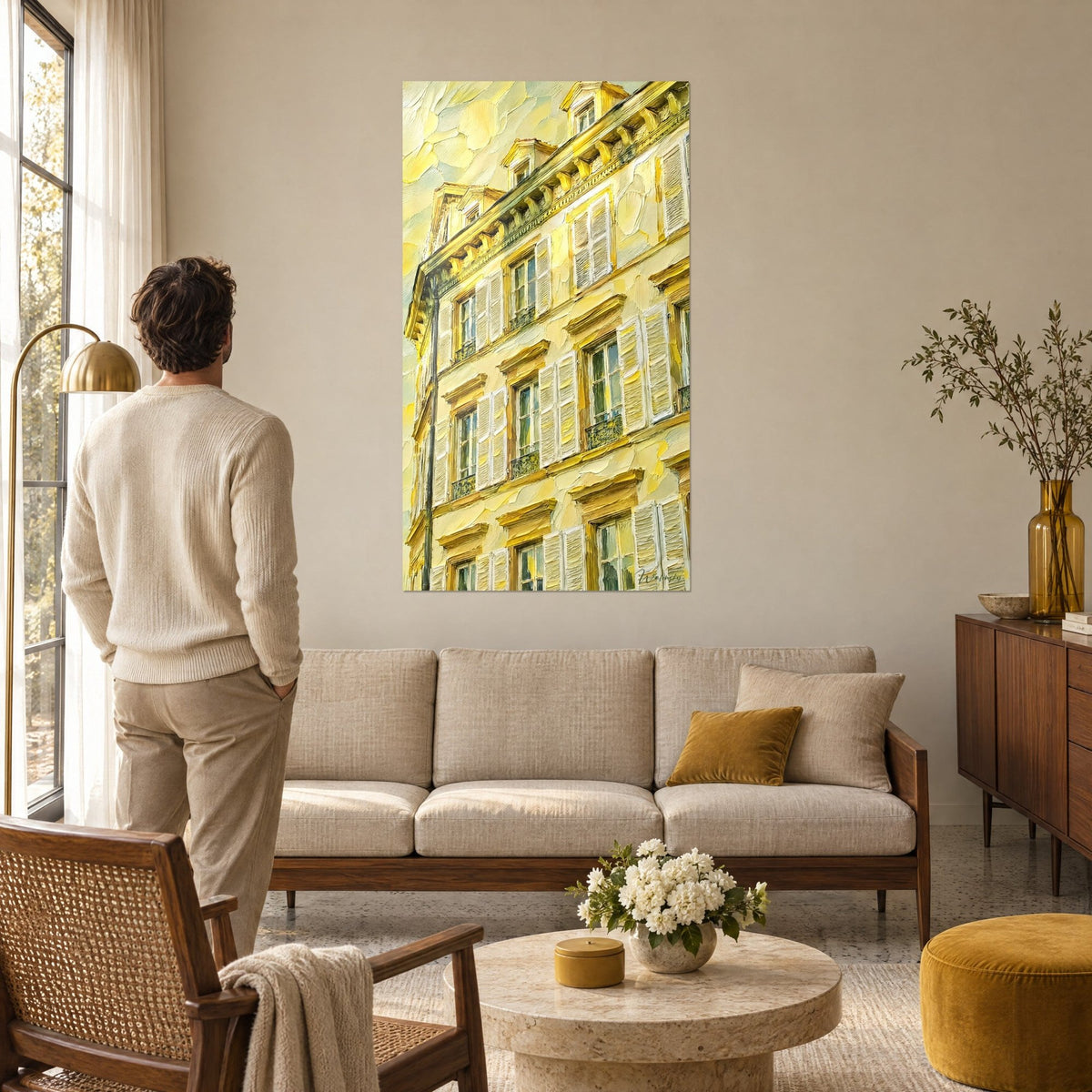 Cuadro fachada de edificio con postigos crema y cornisas doradas, empastes amarillo limón y beige, sobre un sofá en un salón luminoso