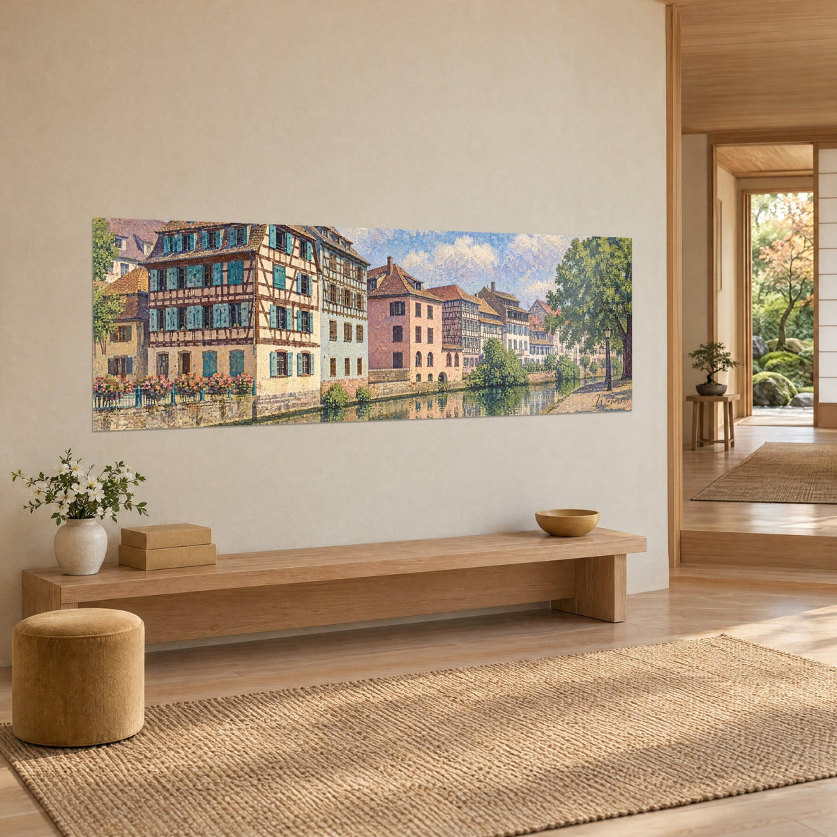 Quadro di una riva fiorita alsaziana: case a graticcio rosa pallido e crema, riflessi verdi nell'acqua, appeso di traverso su una parete beige