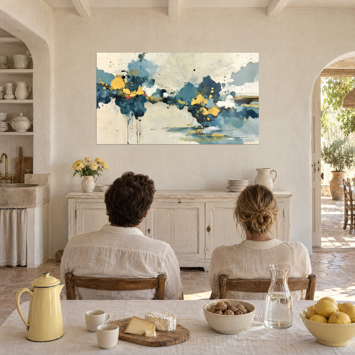 Wall art of a post-storm sky with steel-blue clouds dotted with gold, a couple seen from behind at a table in a Provençal farmhouse