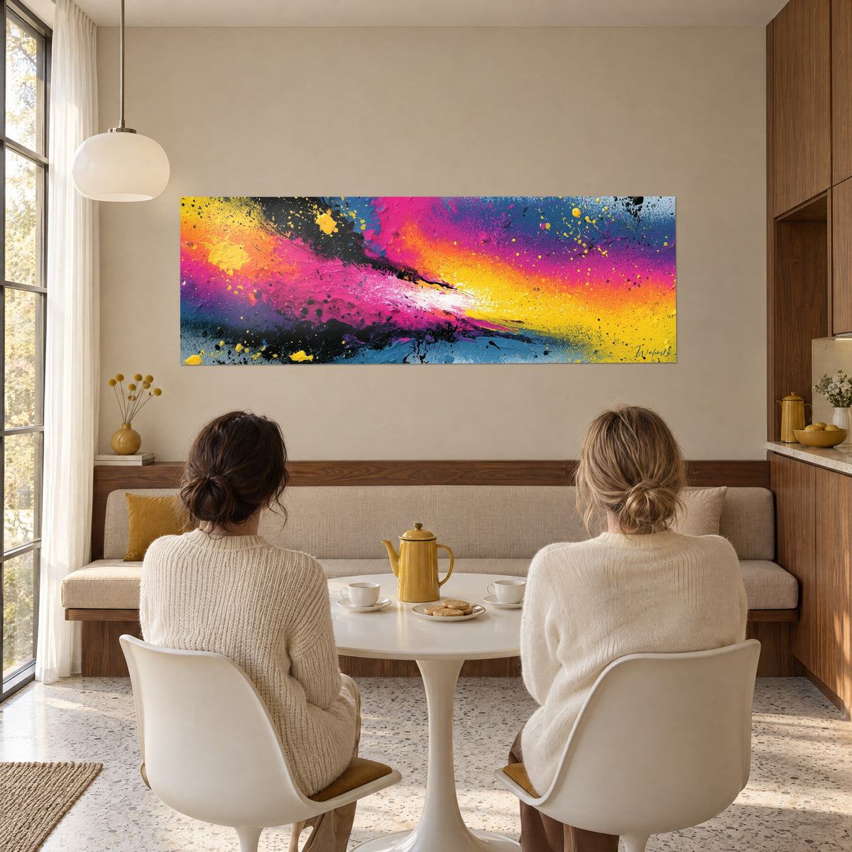Schilderij straal verf in roze, geel en oranje op blauwe achtergrond, zwarte spatjes, bekeken door twee vrouwen aan de eettafel in de woonkamer
