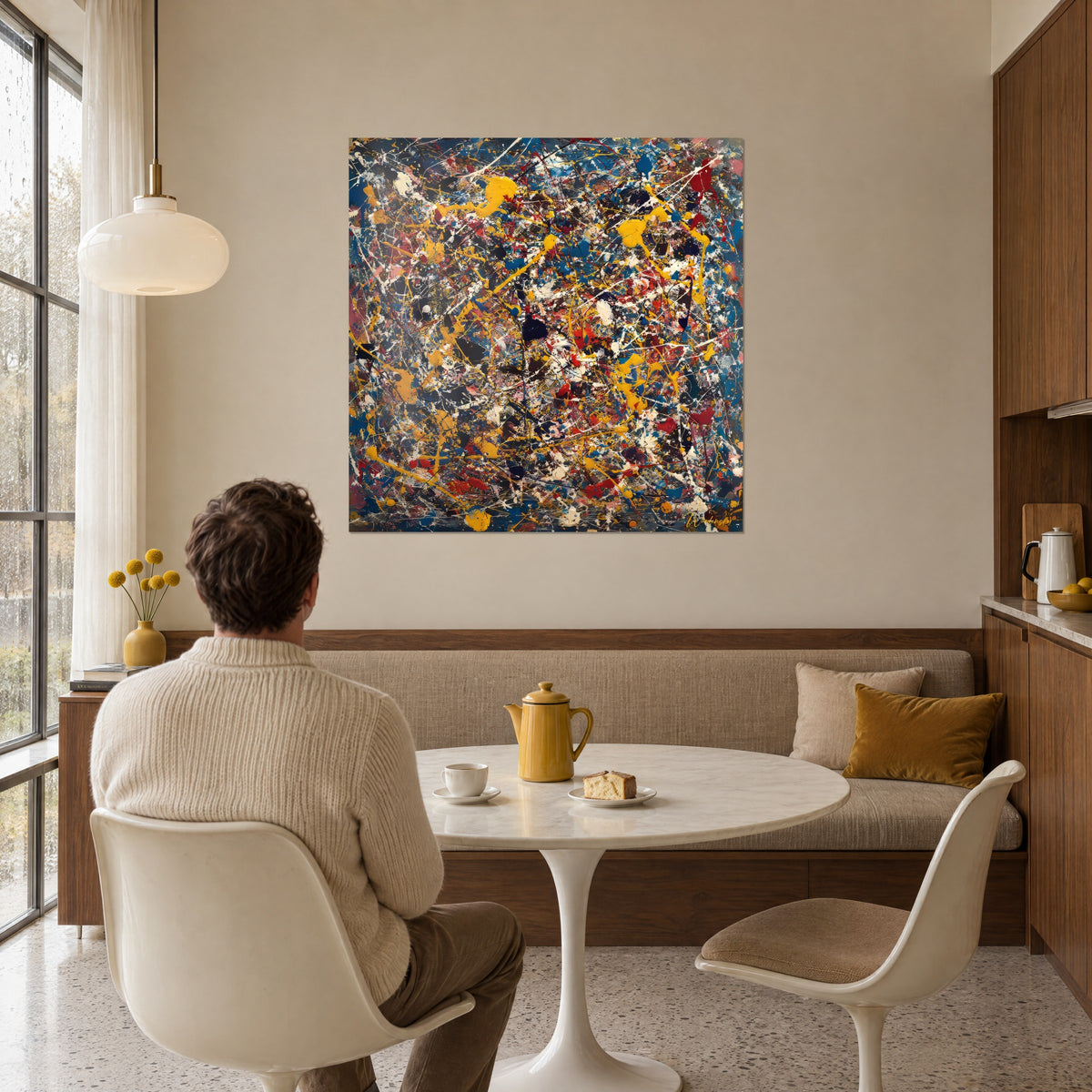 Cuadro lienzo dripping arremolinado en amarillo limón, azul noche y rojo ladrillo, hombre de espaldas sentado a la mesa junto a un banco de comedor