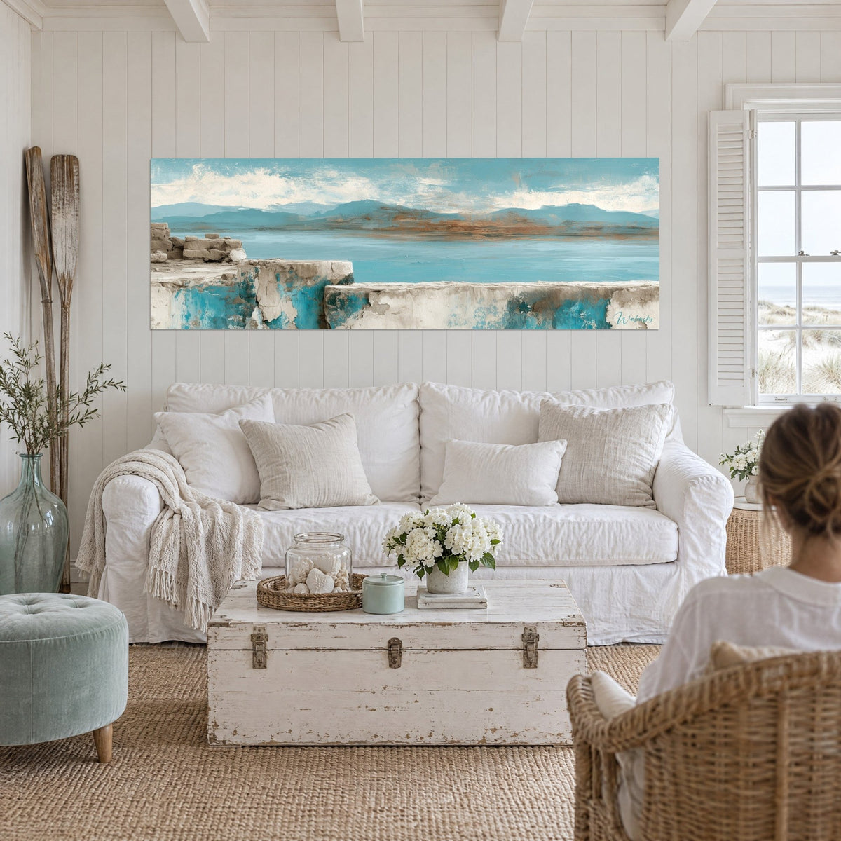 Tableau muret de pierre écaillé face à une mer turquoise, collines bleutées et ocre, au-dessus d'un canapé dans un salon lumineux