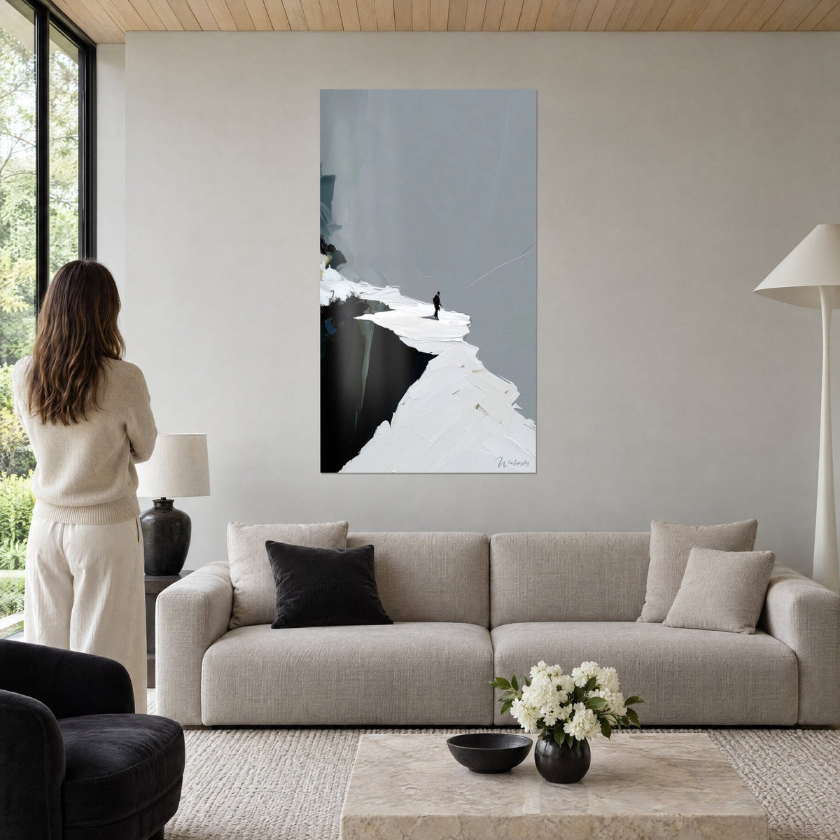 Gemälde schwarze Silhouette im Gleichgewicht auf einem weißen Grat, perlgrauer Himmel und dunkle Felswand, über einem Sofa in einem hellen Wohnzimmer