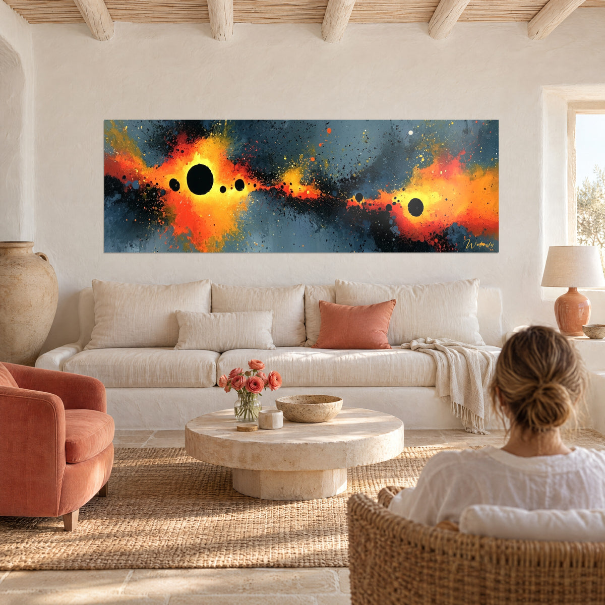 Wall art constellation of black spheres over orange and anthracite splashes, woman seen from behind, above a sofa in a bright living room