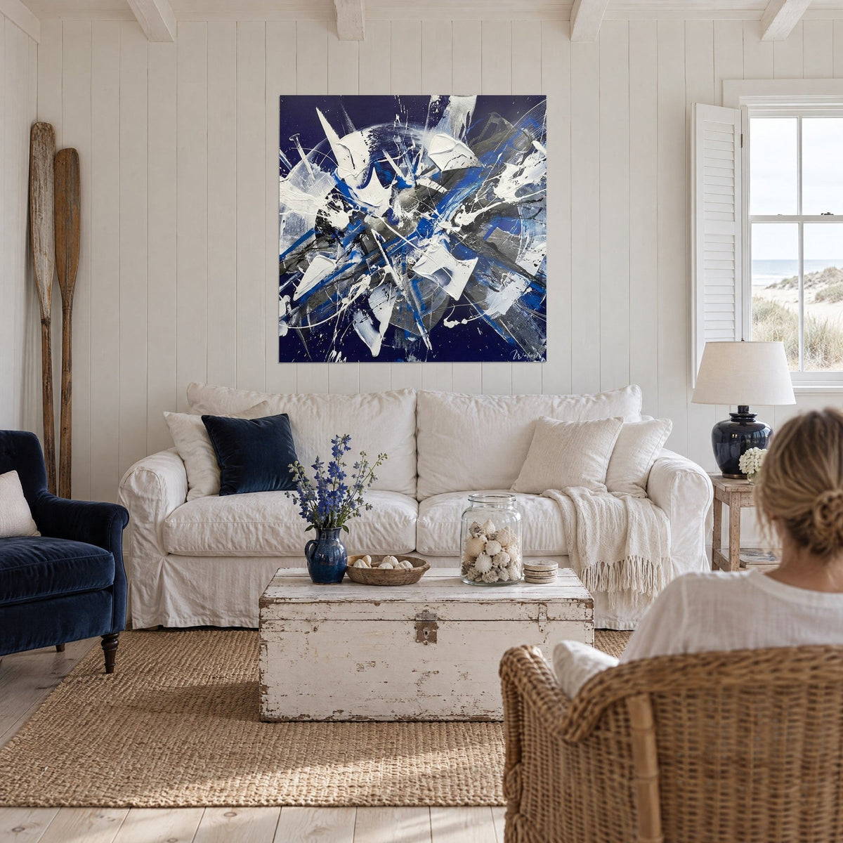 Tableau éclats blancs épais sur fond bleu nuit, striures grises, une femme de dos au-dessus d'un canapé dans un salon lumineux