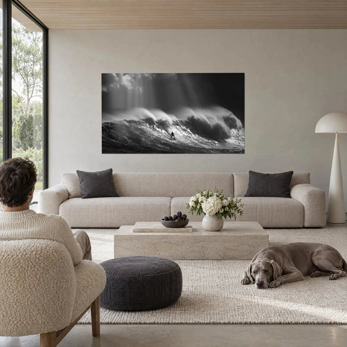 Wall art of a tiny black surfer on a giant grey wave, rays of white light, above a sofa in a bright living room