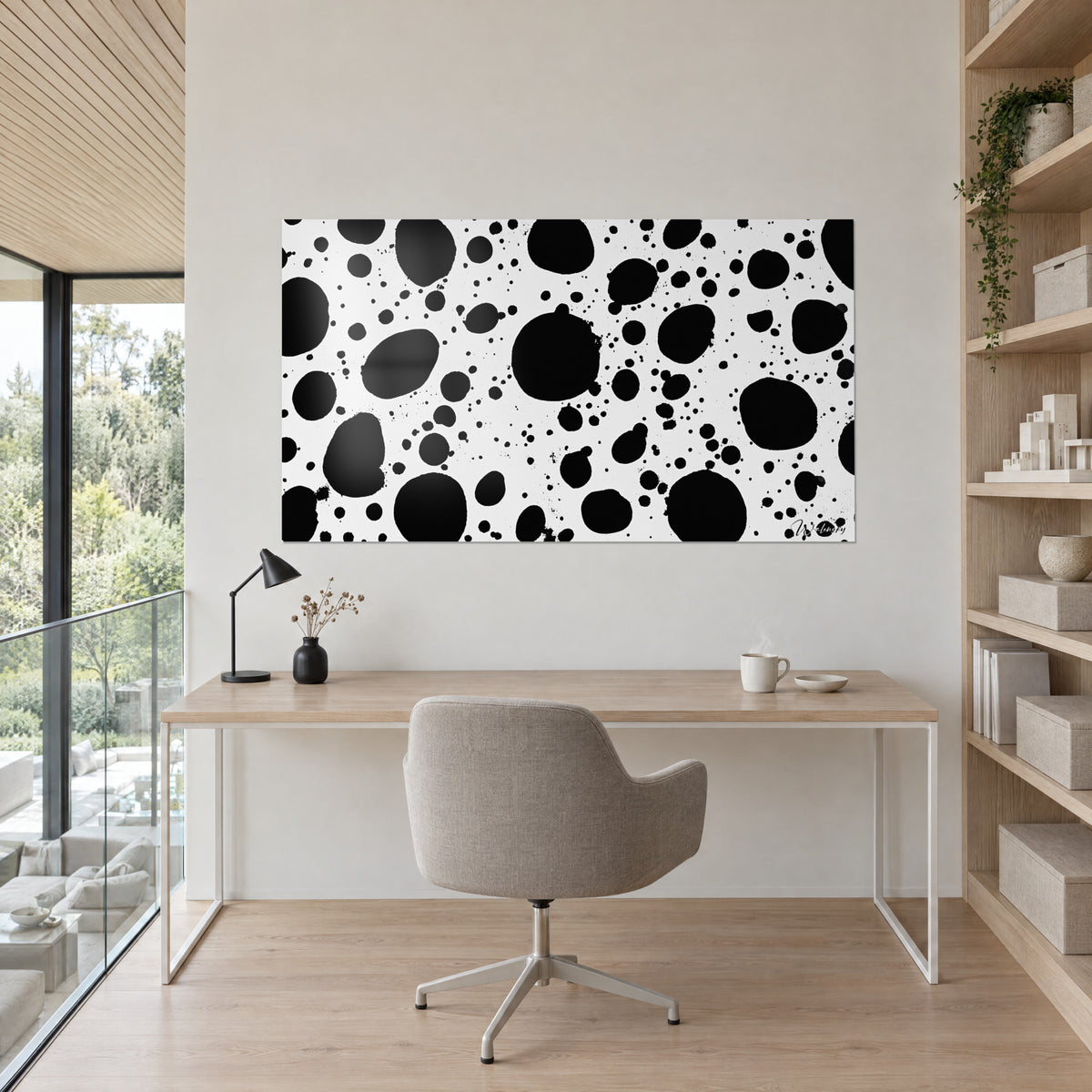 Wall art with a black and white dalmatian-style spotted pattern, beige wall, light wood desk, grey armchair and a well-stocked shelf