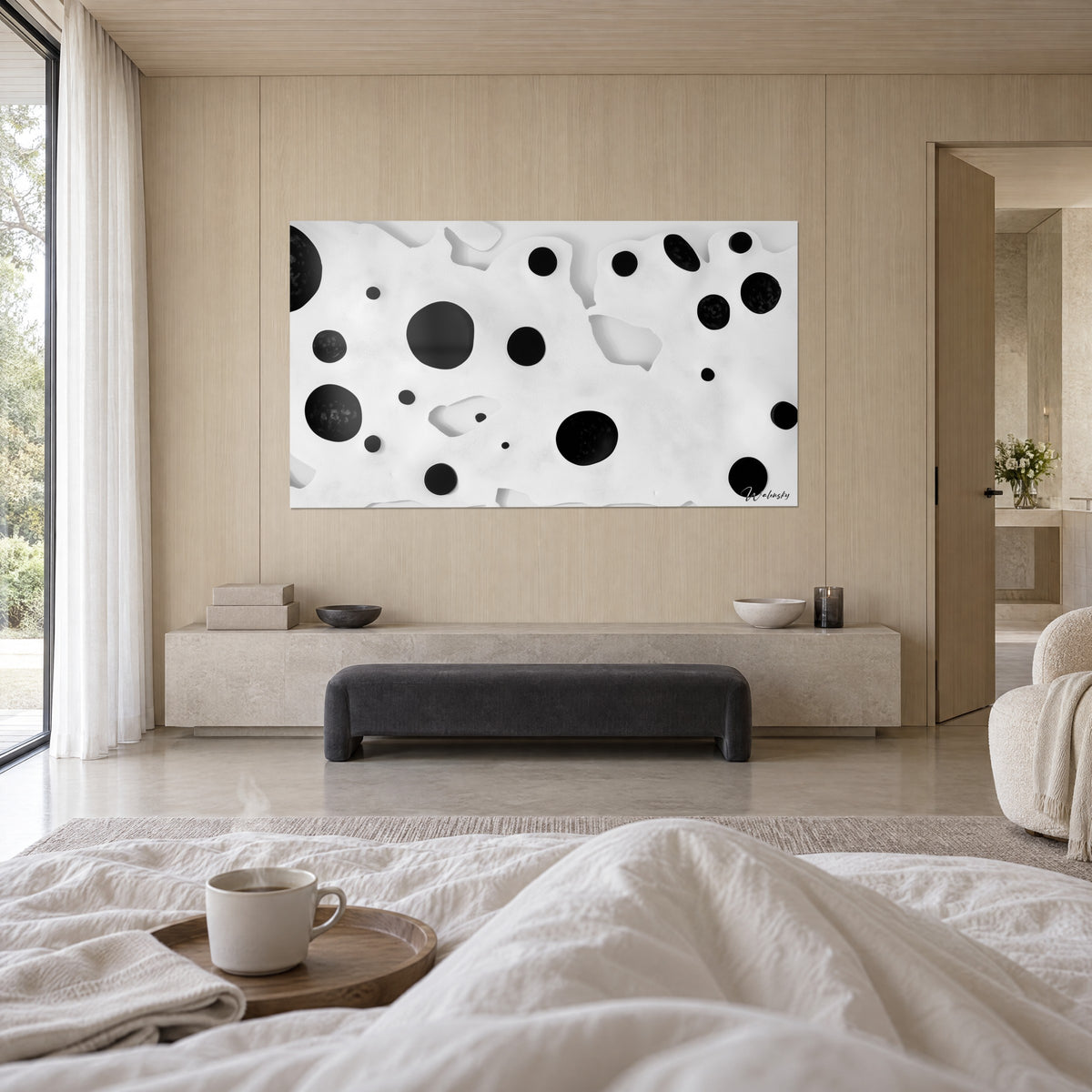 Wall art with deep black circles on a white textured surface, hung above a bed in a bright bedroom, person seen from behind, white throw, light wood panelling