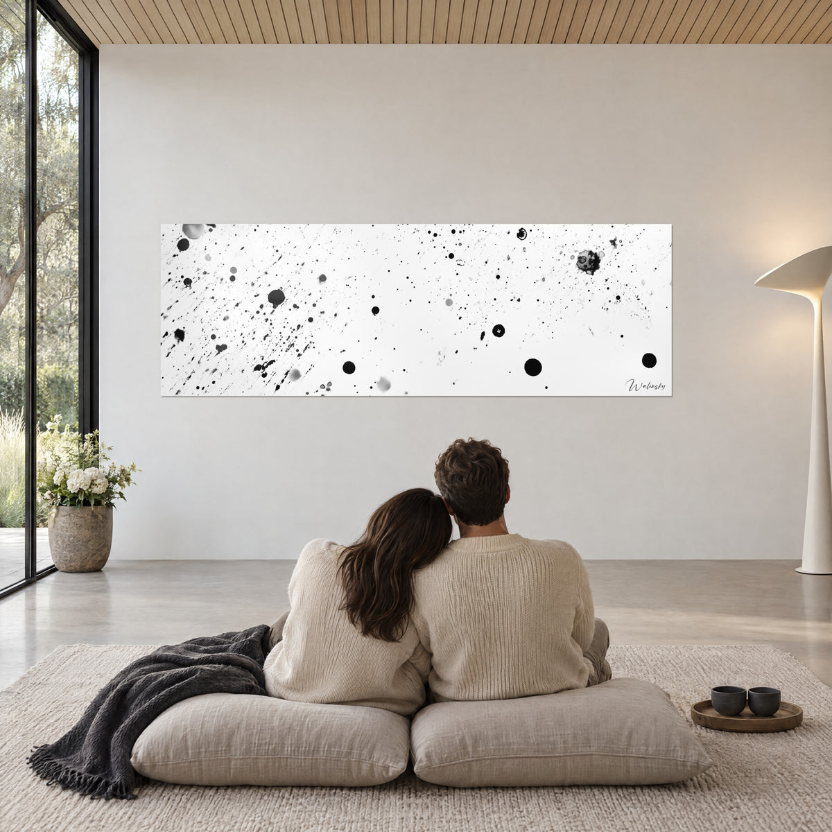 Gemälde mit einem Himmel aus schwarzen und grauen Funken auf weißem Grund, cremefarbene Wand, umschlungenes Paar auf beigen Kissen, anthrazitfarbene Decke, Glasfront