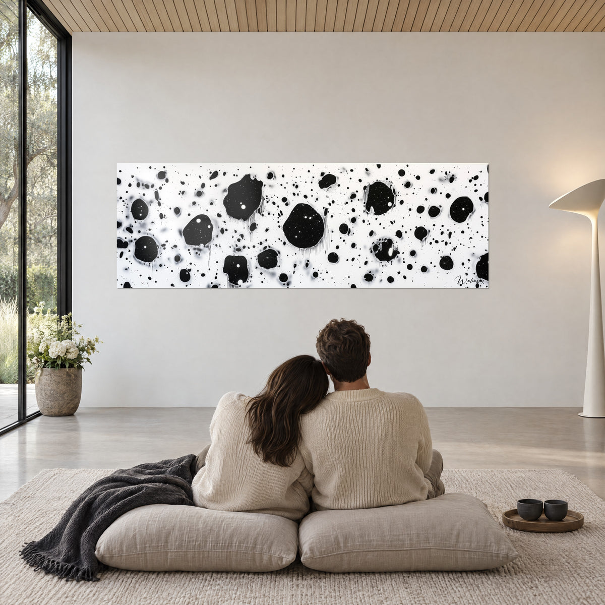 Cuadro de cosmos de manchas negras salpicadas de blanco, aspecto volcánico, frente a una pareja de espaldas sentada sobre cojines beige