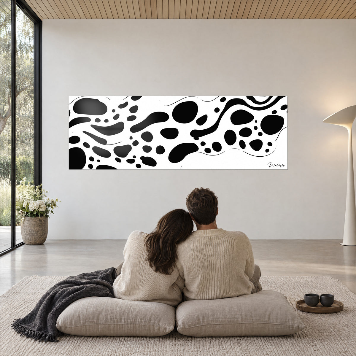 Quadro astrazione di macchie nere su bianco brillante, di fronte a una coppia di spalle su cuscini beige, plaid antracite