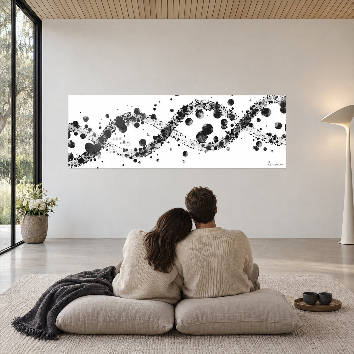 Tableau spirale moléculaire en taches noires et gris argenté sur blanc, face à un couple assis sur des coussins beiges