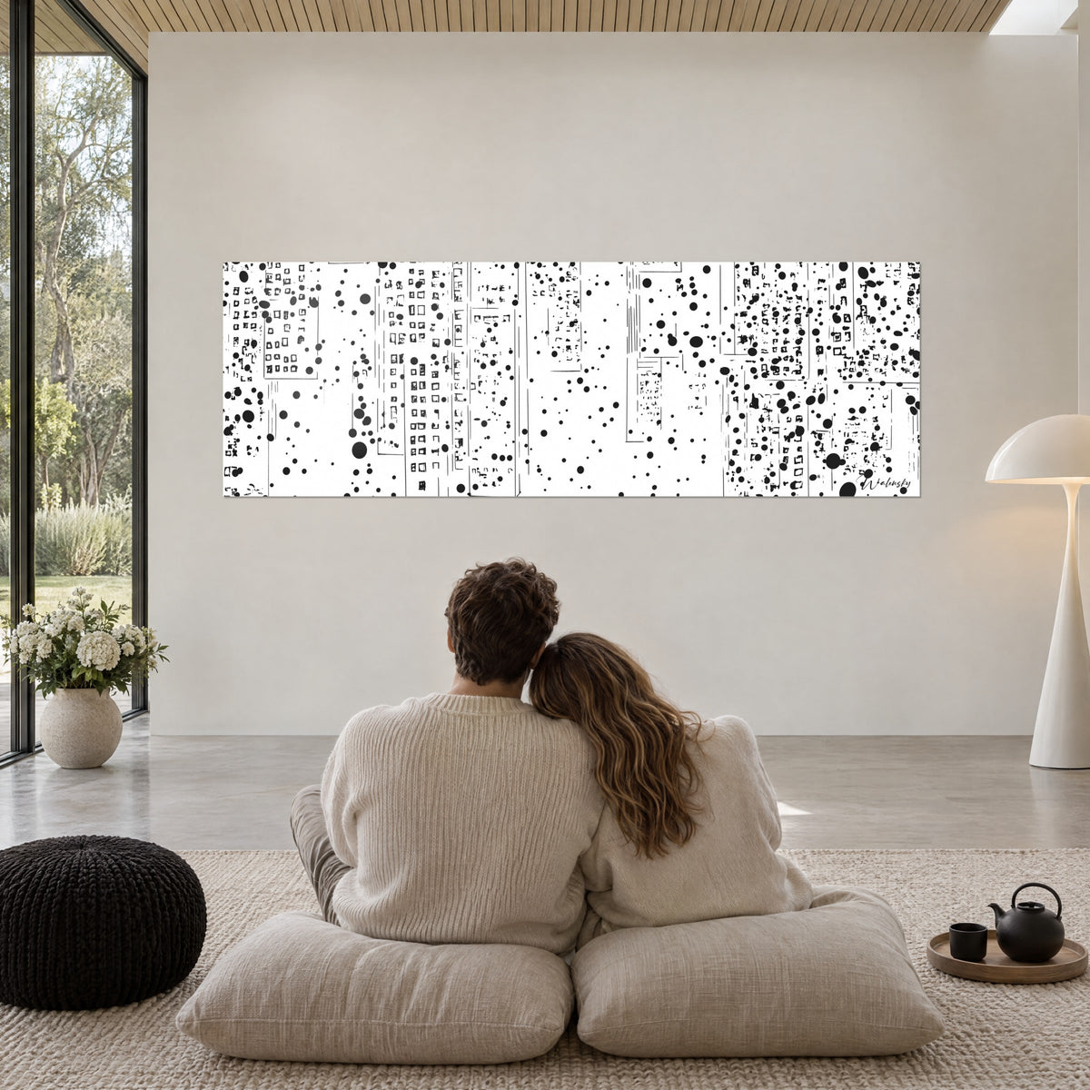 Gemälde abstrakte Skyline, übersät mit schwarzen Flecken auf weißem Grund, Paar eng umschlungen von hinten auf grauen Kissen, cremefarbene Wand