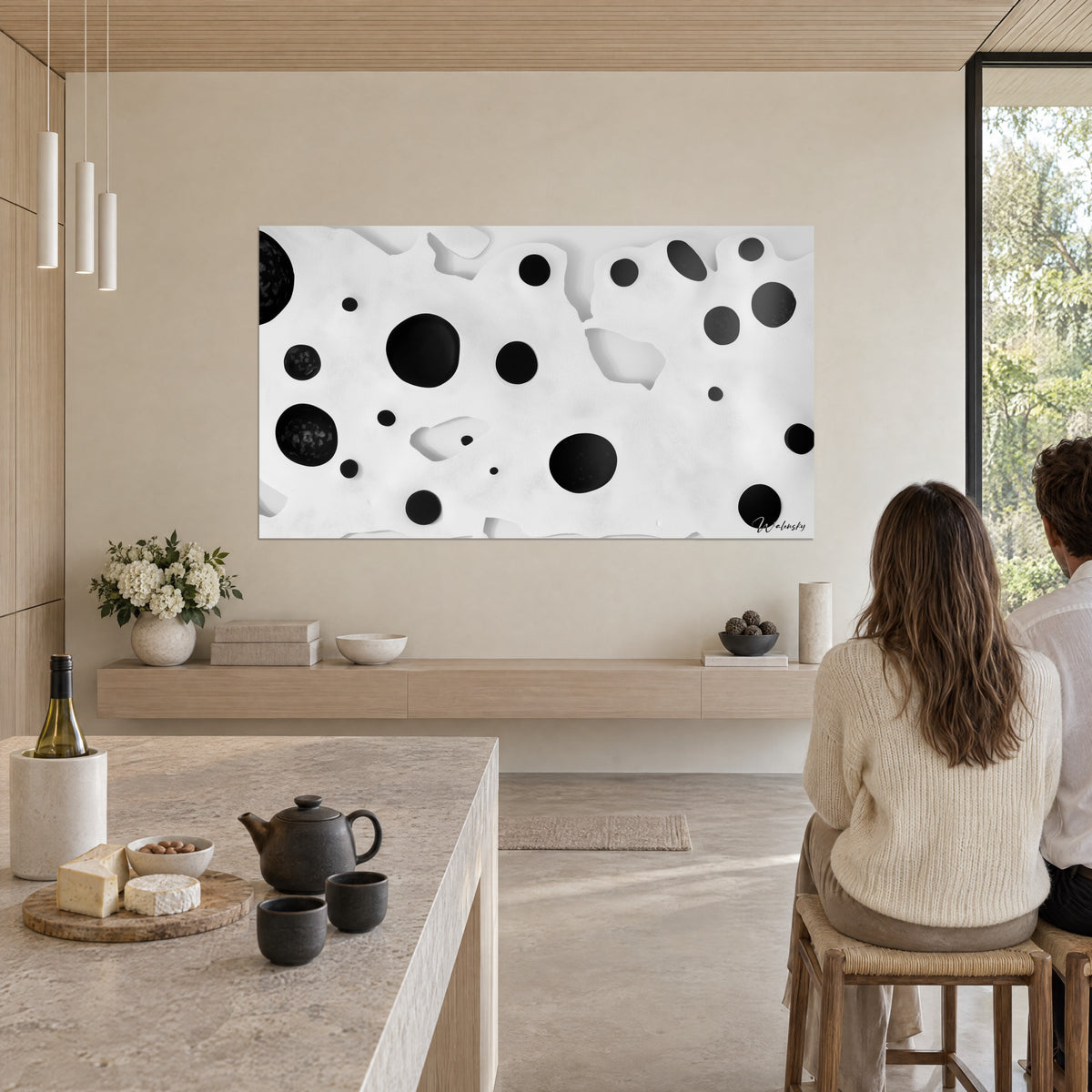 Wall art with a constellation of black dots on a textured white background, couple seen from behind, cream sweater, grey stone island, blonde wood, black teapot