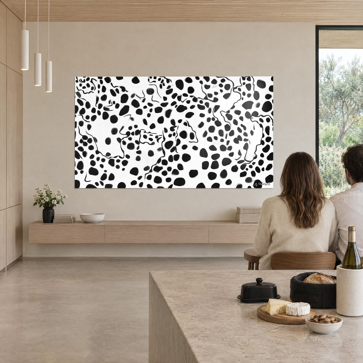 Gemälde mit einer Konstellation aus schwarzen Flecken und feinen Linien auf Weiß, ein Paar von hinten am Tisch sitzend, über einer Konsole aus hellem Holz