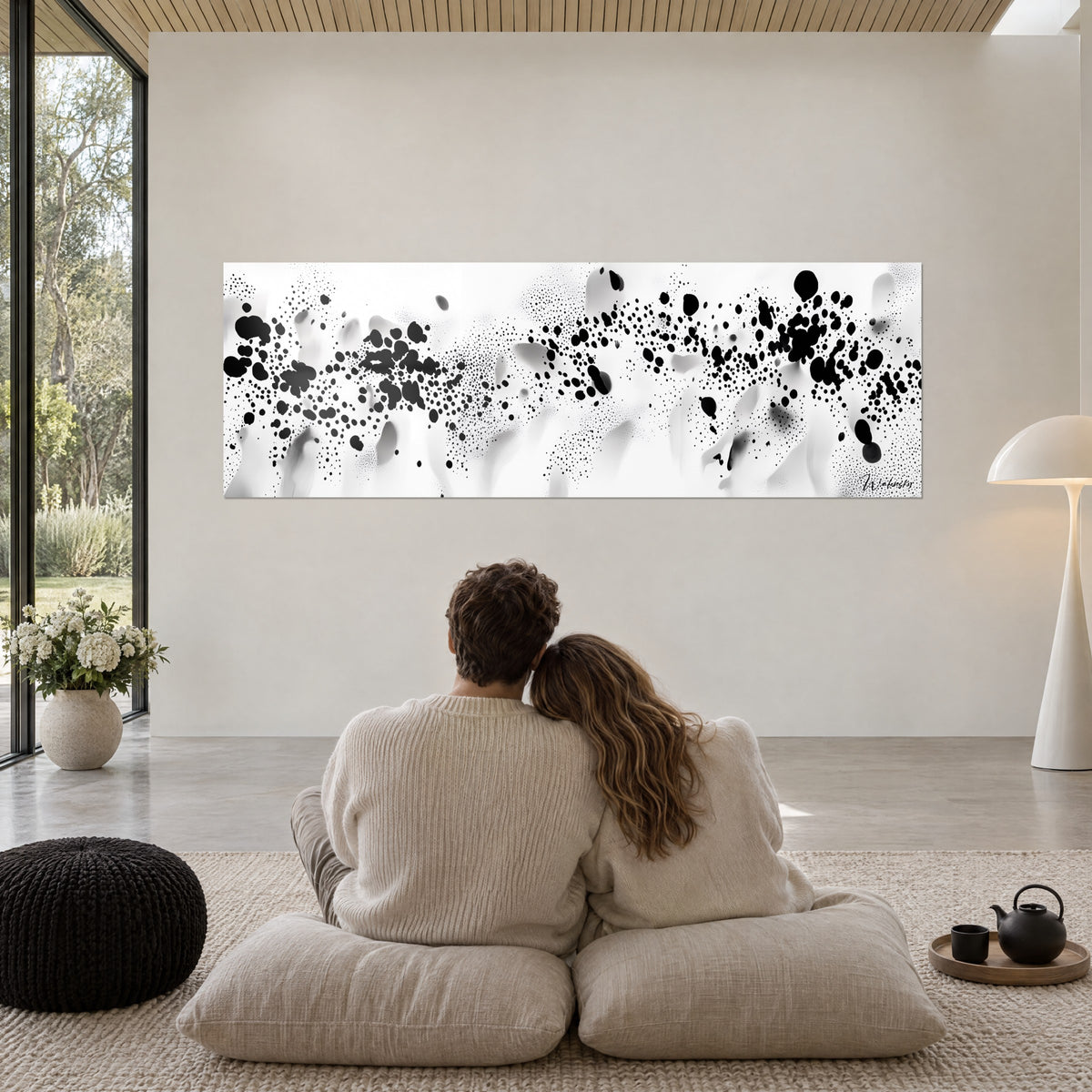 Schilderij met een nevel van zwarte vlekken op een wit, grijs gesluierd achtergrond, omhelzend koppel van achteren op beige poefs, glazen schuifwand