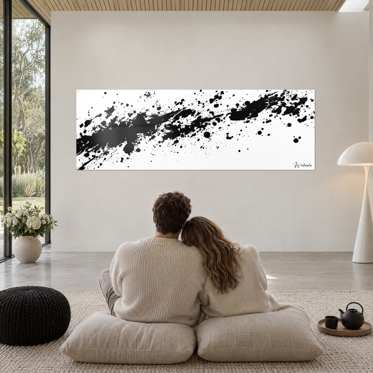 Tableau abstrait noir et blanc tacheté, coulures et gouttes dispersées, couple enlacé de dos sur des poufs beiges dans un salon vitré