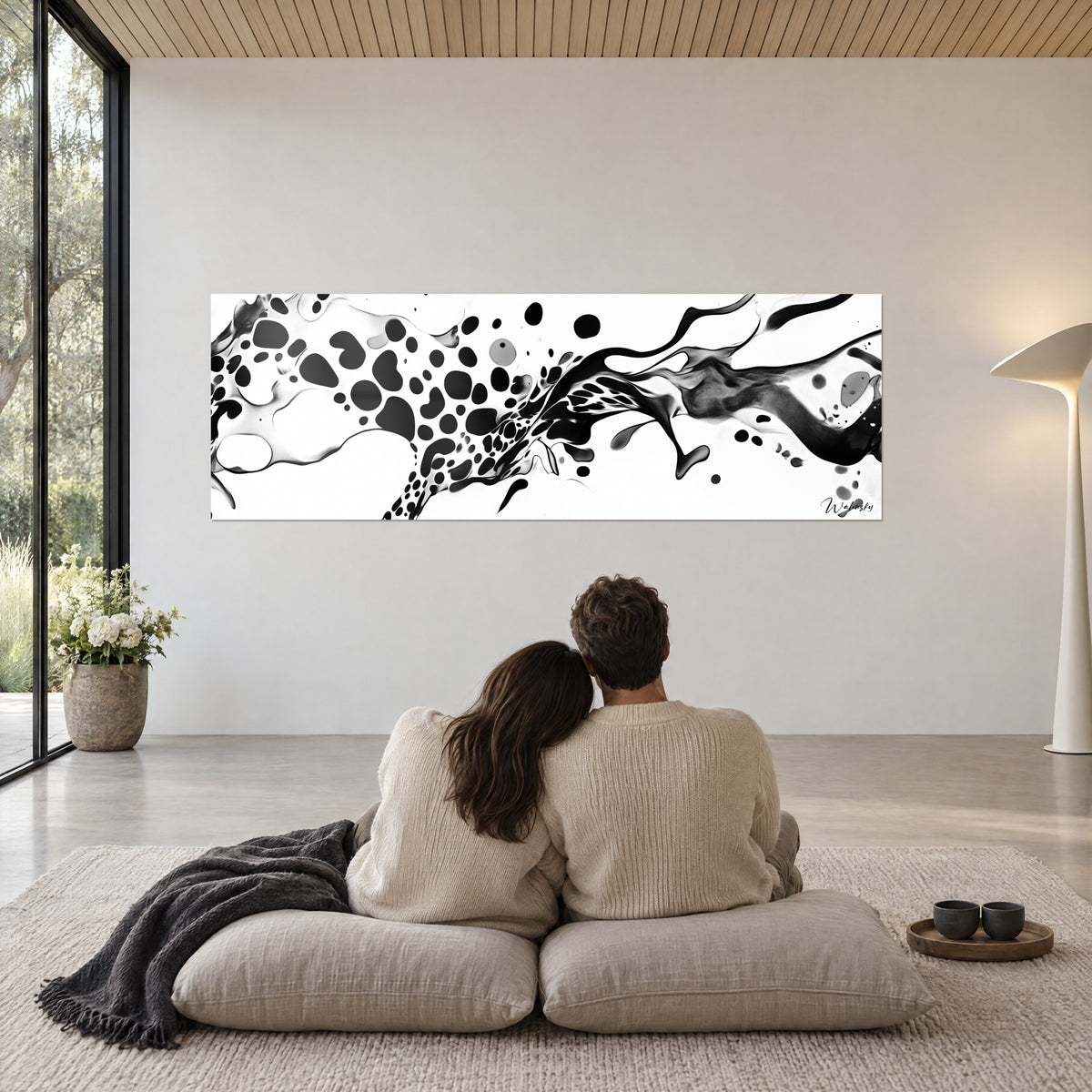 Quadro di colata nera e bianca con gocciolature maculate, coppia di spalle su pouf beige, plaid grigio, soggiorno inondato di luce