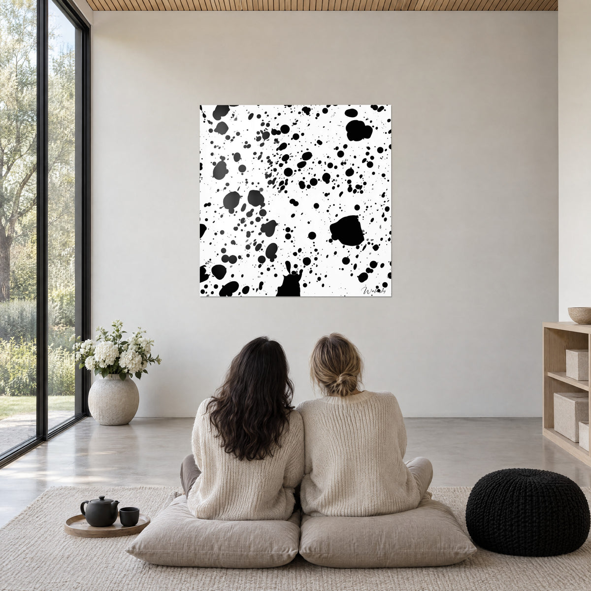Gemälde mit einem Teppich aus schwarzen Flecken auf weißem Grund, große Spritzer und feine Tropfen, an einer beigen Wand über zwei sitzenden Personen