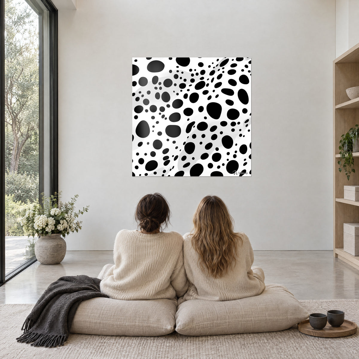 Quadro con motivo cellulare nero su bianco, macchie tonde e gocce, due donne di spalle sedute su cuscini beige e un plaid grigio
